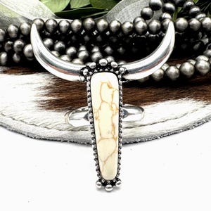 May include: A silver ring with a white stone in the shape of a bull's head. The ring is set on a white and brown fur background.