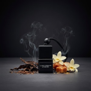 May include: A black square glass fragrance diffuser bottle with a black cap and hanging cord, labeled Vanilla Tobacco & Caramel. It is surrounded by dried tobacco leaves, two white vanilla flowers, and caramel cubes with wisps of smoke.