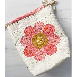 May include: A quilted drawstring bag project with a large floral design. The bag is white with gold polka dots and a large flower in shades of pink and orange. Finished size is 11" x 14" x 4". The text "Mini Bloomberg Drawstring Bag Project" is at the top.