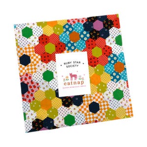 May include: A colorful patchwork fabric square with a floral hexagon pattern in various colors, including red, yellow, green, and blue. A white card with the text "RUBY STAR SOCIETY" and "eatnap" is placed on top. The fabric is likely for quilting or crafting.