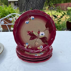 May include: Set of four red and white floral patterned dinner plates. The plates have a scalloped edge and are stacked on top of each other.