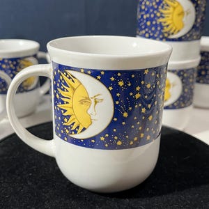 May include: Set of six white ceramic mugs with a blue and gold design featuring a sun and moon with stars.