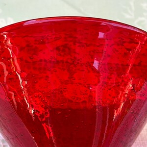 May include: Close-up of a vibrant red glass. The glass has a conical shape and is filled with tiny bubbles, creating a textured appearance. The color is a deep, rich red, with light reflecting off the surface.