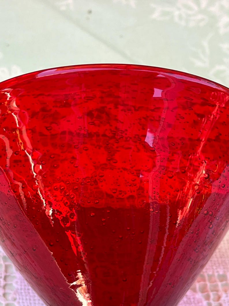 May include: Close-up of a vibrant red glass. The glass has a conical shape and is filled with tiny bubbles, creating a textured appearance. The color is a deep, rich red, with light reflecting off the surface.