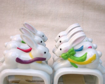 May include: Set of six white ceramic bunny napkin rings. Each bunny has a different colored ribbon around its neck. The ribbons are purple, red, green, blue, yellow, and pink.