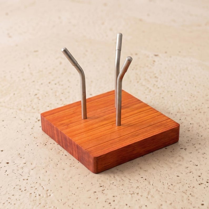 Op de afbeelding: Een houten displaystandaard met een vierkante basis en drie metalen staven. De basis is roodbruin van kleur met zichtbare houtnerf. De metalen staven zijn zilverkleurig en hebben gebogen en rechte secties.