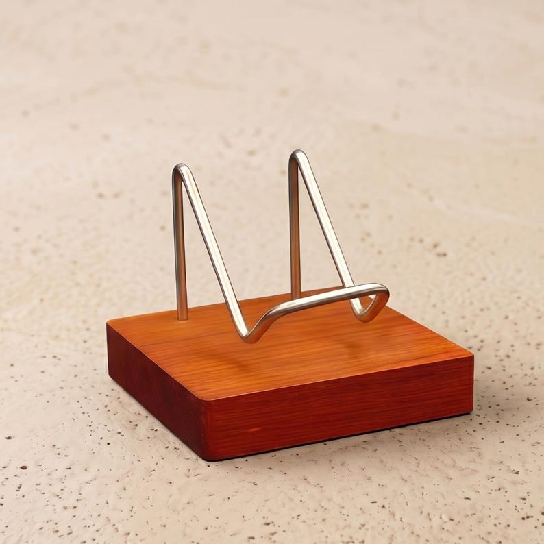 Op de afbeelding: Een kleine, vierkante houten displaystandaard met een roodbruine afwerking. Het heeft een zilverkleurige metalen ezel-achtige steun. De standaard is ontworpen om kleine decoratieve items, borden of kunstwerken te bevatten.