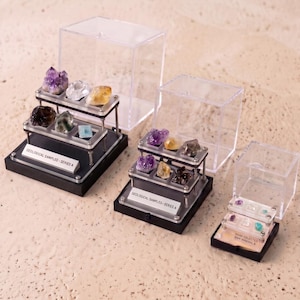 Op de afbeelding: Drie gelaagde vitrines met ruwe mineraalmonsters. De twee grotere kasten zijn gelabeld met GEOLOGICAL SAMPLES - SERIES A, terwijl de kleinste kast is gelabeld met HAND COLLECTED RAW MINERALS. Elke kast is voorzien van doorzichtige acryldeksels.