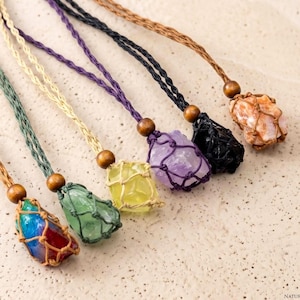 Può includere: Una collezione di collane con pietre preziose con pietre di vari colori, tra cui verde, giallo, viola e arancione. Ogni pietra è racchiusa in una rete intrecciata e sospesa a un cordino con una perla di legno.