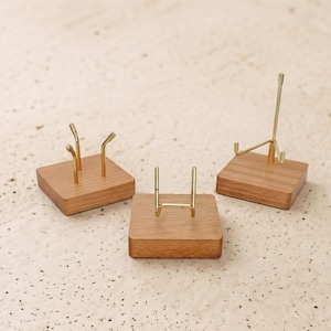 Op de afbeelding: Drie kleine display stands. Elke stand heeft een vierkante houten basis met een goudkleurige metalen steun. De steunen hebben verschillende ontwerpen, waaronder een vork met twee tanden, een eenvoudige boog en een klein ezel.