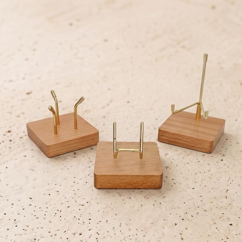 Op de afbeelding: Drie kleine display stands. Elke stand heeft een vierkante houten basis met een goudkleurige metalen steun. De steunen hebben verschillende ontwerpen, waaronder een vork met twee tanden, een eenvoudige boog en een klein ezel.