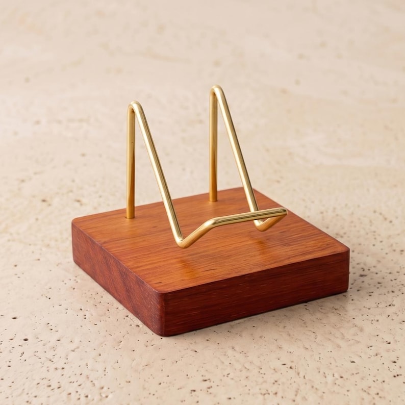 Op de afbeelding: Een houten displaystandaard met een rechthoekige basis en een goudkleurig metalen frame. Het frame heeft een driehoekige vorm, ontworpen om een bord of ander decoratief item vast te houden. Het hout heeft een rijke, roodbruine kleur.