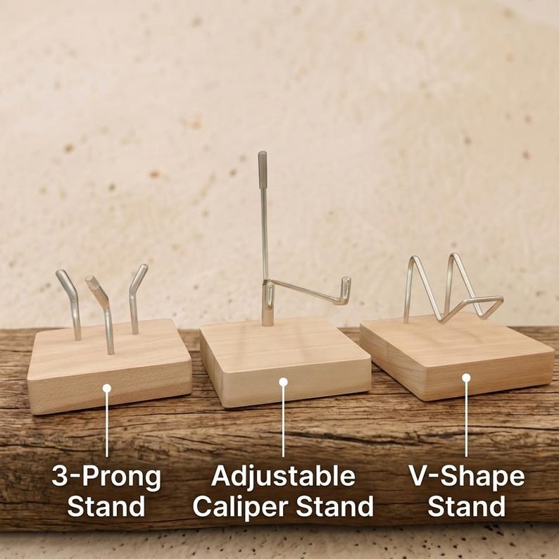Op de afbeelding: Drie houten display stands met metalen steunen. De stands zijn gelabeld: "3-Prong Stand", "Adjustable Caliper Stand" en "V-Shape Stand". De stands staan op een houten oppervlak.