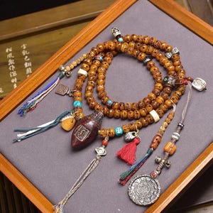 以下が含まれることがあります： 琥珀色のビーズネックレスと装飾ペンダントのコレクション。ネックレスは彫刻されたビーズ、ターコイズのアクセント、さまざまなチャームが特徴です。小さな濃い赤色の彫刻ペンダントと銀貨のようなペンダントも含まれています。