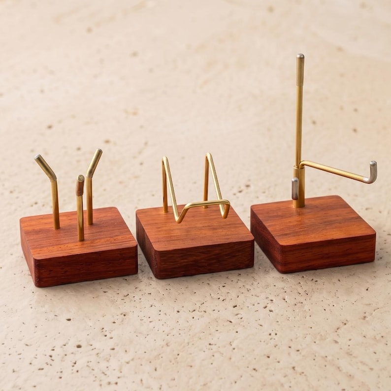Op de afbeelding: Drie houten displaystandaards met messing metalen accenten. De standaards hebben een vierkante basis en zijn ontworpen om verschillende items vast te houden. De standaards zijn gemaakt van donker hout en hebben een natuurlijke afwerking. De metalen accenten zijn goudkleurig.