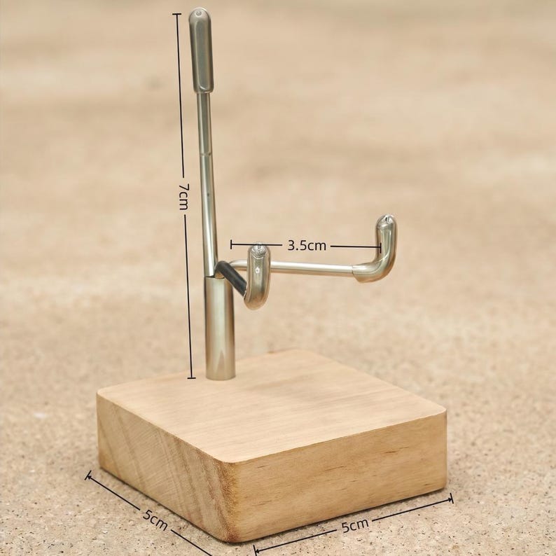 Op de afbeelding: Een displaystandaard met een houten basis van 5 cm bij 5 cm. Een zilveren metalen arm strekt zich 7 cm omhoog uit, met een gebogen haak van 3,5 cm. De standaard is ontworpen om een item vast te houden.