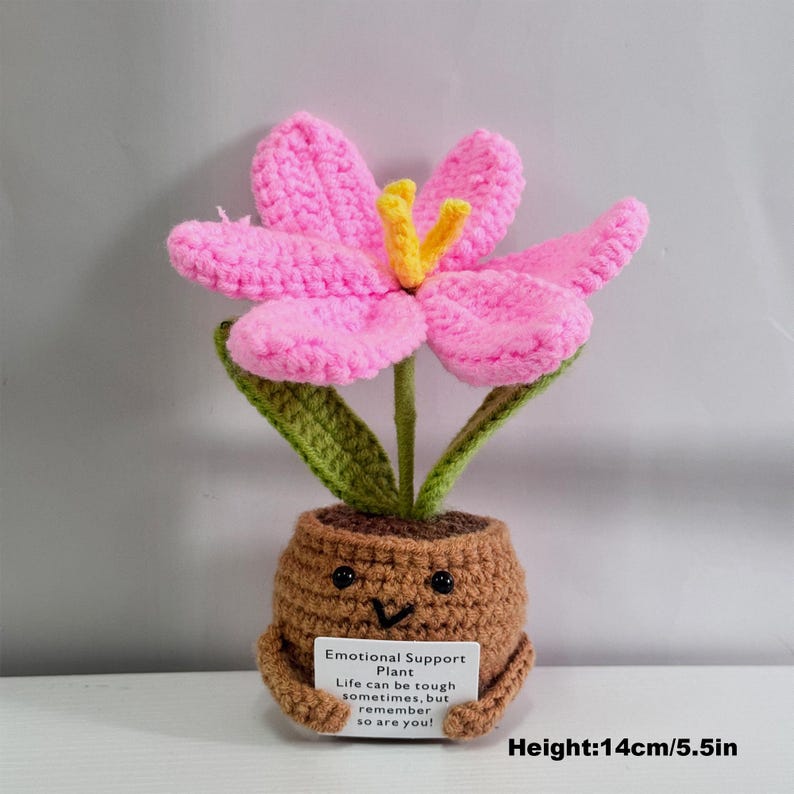May include: A crocheted pink flower with yellow center in a brown pot with a smiling face. The pot is holding a card that reads "Emotional Support Plant. Life can be tough sometimes, but remember so are you!" The plant is 5.5 inches tall.