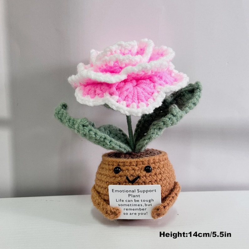May include: Crocheted pink and white flower in a brown pot with a smiling face. The pot is holding a card that reads "Emotional Support Plant. Life can be tough sometimes, but remember so are you!" The plant is 5.5 inches tall.