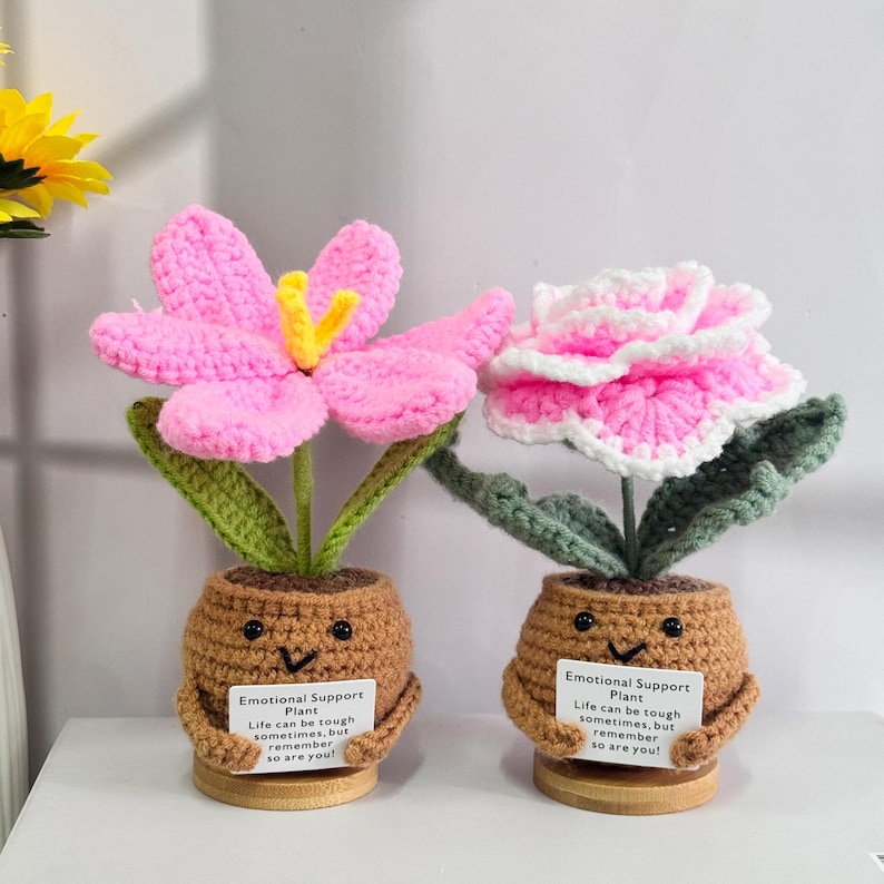 May include: Two crocheted flower plants in brown pots with happy faces. Each plant has a sign that reads "Emotional Support Plant. Life can be tough sometimes, but remember so are you!"