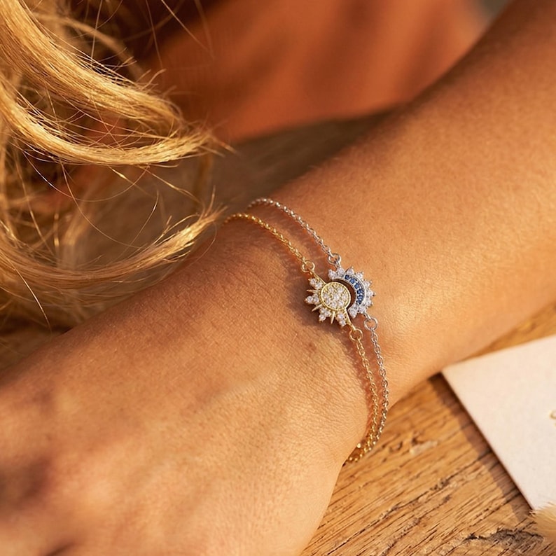 May include: Two delicate bracelets with sun and moon charms. One bracelet is gold-toned with a sun charm, the other is silver-toned with a moon charm. The charms are embellished with small, sparkling stones.