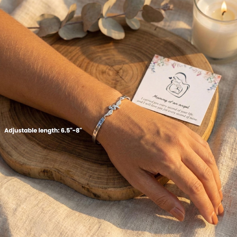 May include: A silver bracelet with a knot design and the words "Mommy of" engraved on it. The adjustable bracelet is 6.5"-8" long. A card with the text "Mommy of an angel" is next to the bracelet.