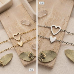 May include: Two heart-shaped bracelets, one gold and one silver, are displayed. The gold bracelet features a hollow heart and a solid heart charm. The silver bracelet has a hollow heart and a solid heart charm. Both are on a chain.