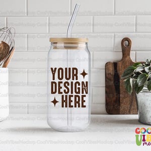 Op de afbeelding: Een glazen pot met een houten deksel en een rietje. De pot heeft de tekst "YOUR DESIGN HERE" erop gedrukt. De pot staat op een wit aanrecht.