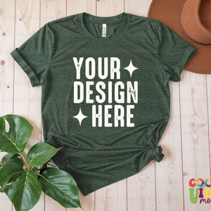 May include: A dark green t-shirt with a white distressed text design that says "YOUR DESIGN HERE" on a wood background.