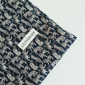 May include: Black fabric with a white leopard print pattern. The fabric has a white tag with the text "LILY & DAISY" on it.
