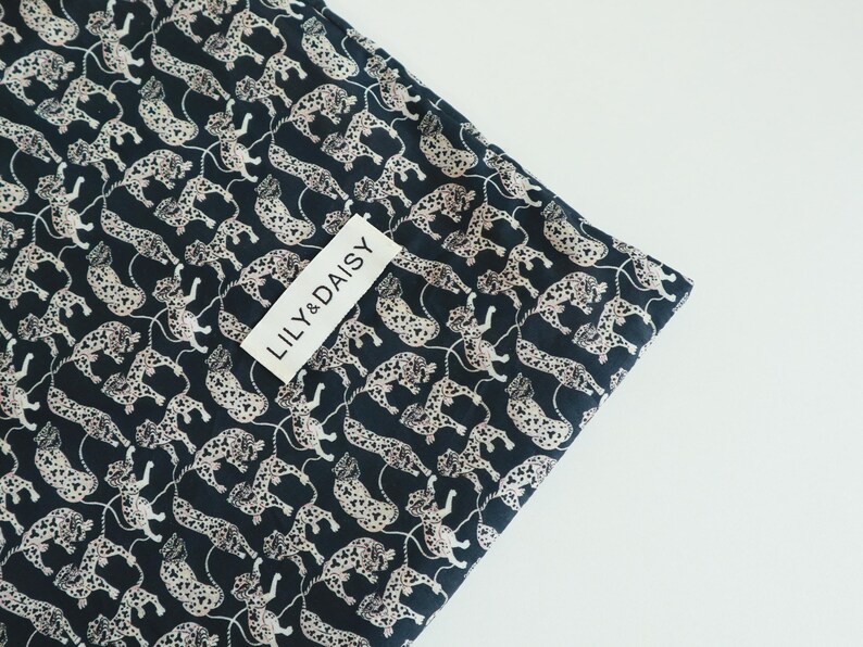 May include: Black fabric with a white leopard print pattern. The fabric has a white tag with the text "LILY & DAISY" on it.