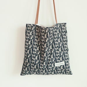 May include: A black tote bag with a white and brown animal print design. The bag has brown leather straps and a white label that says "LILY&DAISY".