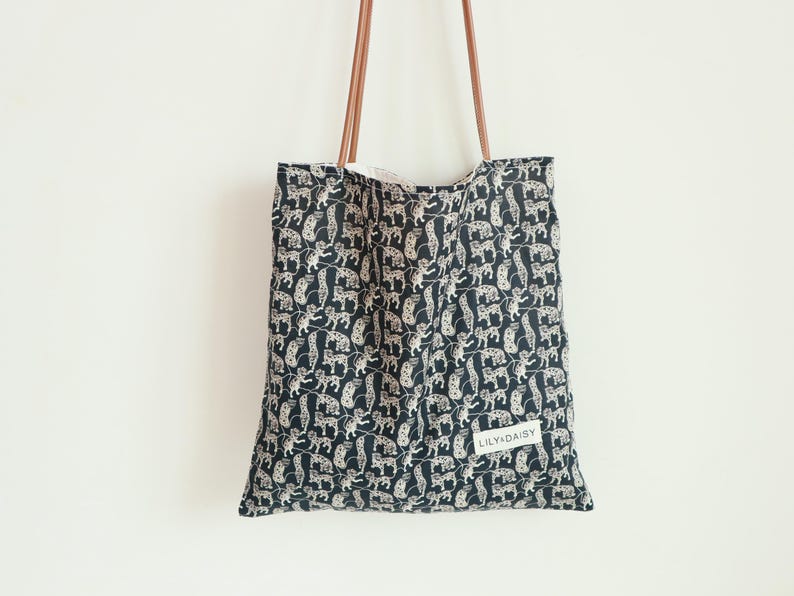 May include: A black tote bag with a white and brown animal print design. The bag has brown leather straps and a white label that says "LILY&DAISY".
