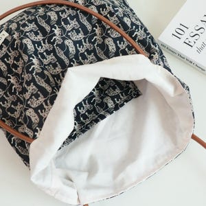May include: A black tote bag with a white leopard print design. The bag has brown leather handles and a white cotton lining. The bag is open and the lining is visible.