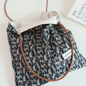 May include: A black and white tote bag with a leopard print design. The bag has brown leather straps and a white cotton lining. The bag has a label that says "Lily &  Daisy".