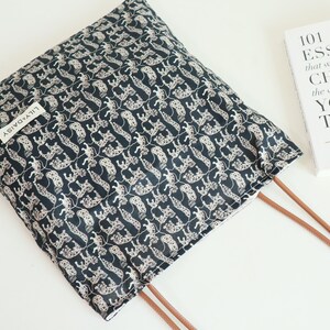 May include: A black tote bag with a white and black leopard print design. The bag has brown straps and a white label that says "Lily & Daisy".