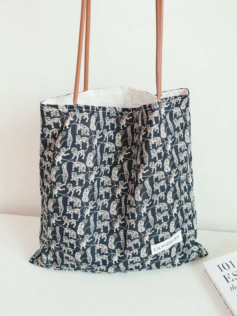 May include: Black tote bag with a white leopard print and brown leather straps. The bag has a white label with the text "LILY&DAISY" on it.