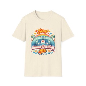 May include: Cream-coloured t-shirt with a colourful graphic. The graphic features two blue manatees kissing under a rainbow, with the text "Stop mana-teasing me". Decorative elements include hearts, palm trees, and flowers.