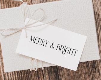 May include: A white gift box with a white tag tied with twine. The tag has the text "Merry & Bright" written in black.