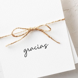 May include: A white card with a simple brown twine bow and the word "gracias" written in black cursive.