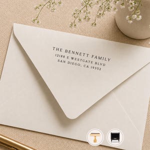 May include: A cream-colored envelope featuring black printed text that reads THE BENNETT FAMILY, 12188 E WESTGATE BLVD, SAN DIEGO, CA 19352. The envelope has a triangular flap and is displayed alongside two small circular icons showing a stamp.