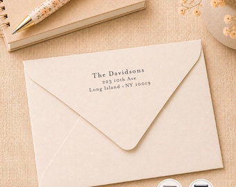 May include: A cream-colored envelope featuring black printed text that reads The Davidsons, 223 10th Ave, Long Island, NY 10019. The envelope is positioned below a spiral-bound notebook and a floral patterned pen, with two small circular product icons.
