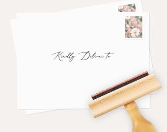 May include: White envelopes with floral stamps and the text "Kindly Deliver To" in elegant script. A wooden stamp with a black ink pad is positioned near the envelopes, ready for use. The image has a soft, neutral color palette.