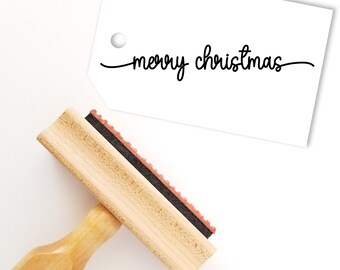 May include: A wooden stamp with a black ink pad and a handle. The stamp reads "merry christmas" in a cursive font.