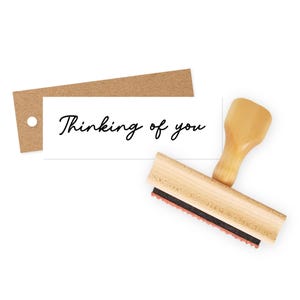 May include: A wooden stamp with a brown handle and a black ink pad. The stamp reads "Thinking of you" in a cursive font.