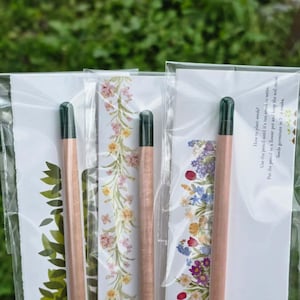 A person's hand holding a customized eco-friendly pencil favor decorated with green leaf illustrations and a wedding date.