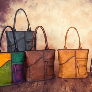 May include: Four leather tote bags in various colors, including black, brown, and a multi-colored bag with orange, green, and purple panels. Each bag has a top handle and a front pocket. The bags are displayed on a wooden surface.