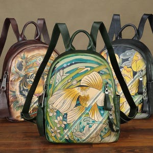 May include: Three leather backpacks with unique hand-painted designs. The first backpack features a tiger, the second a goldfish, and the third yellow flowers. Each has a top handle, adjustable straps, and a zippered front pocket.