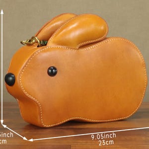 May include: A tan leather handbag shaped like a rabbit. The bag is 9.05 inches (23 cm) long, 5.11 inches (13 cm) high, and 2.75 inches (7 cm) wide. It has black button eyes and a gold-colored clasp.