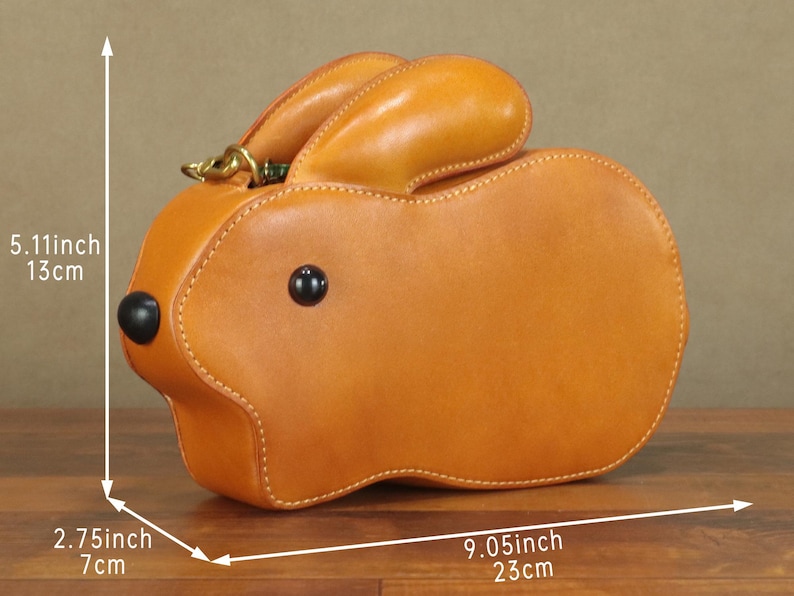 May include: A tan leather handbag shaped like a rabbit. The bag is 9.05 inches (23 cm) long, 5.11 inches (13 cm) high, and 2.75 inches (7 cm) wide. It has black button eyes and a gold-colored clasp.
