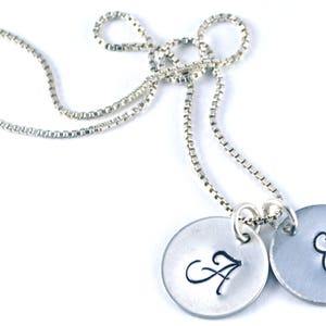 May include: A silver chain necklace with two silver disc pendants. The pendants are engraved with the letters "A" and "E" in a cursive font.